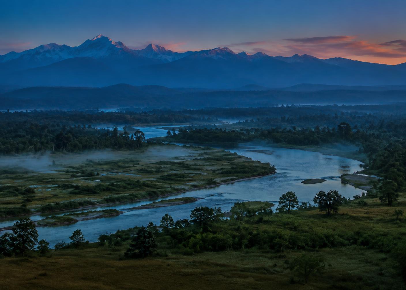 Grassland and forest beneath Himalayan foothills at dusk